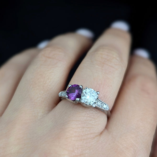 This exquisite vintage toi et moi ring beautifully captures the romanticism of the classic two-stone design, a symbol of two souls intertwined. The ring showcases an old European cut diamond paired with a lovely purplish- pink sapphire. Toi et moi jewelry, historically popularized in the 18th and 19th centuries, gained significant prominence when Napoleon Bonaparte gifted Josephine a similar ring, forever embedding this style in the narrative of love and partnership. Today, this design is a popular choice f