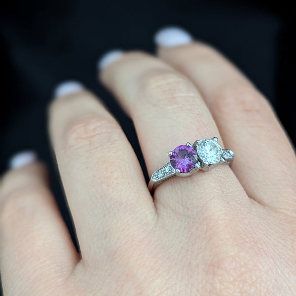 This exquisite vintage toi et moi ring beautifully captures the romanticism of the classic two-stone design, a symbol of two souls intertwined. The ring showcases an old European cut diamond paired with a lovely purplish- pink sapphire. Toi et moi jewelry, historically popularized in the 18th and 19th centuries, gained significant prominence when Napoleon Bonaparte gifted Josephine a similar ring, forever embedding this style in the narrative of love and partnership. Today, this design is a popular choice f