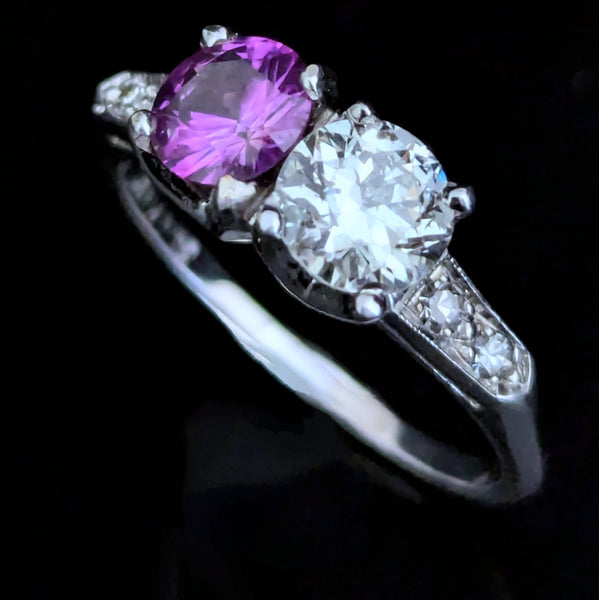 This exquisite vintage toi et moi ring beautifully captures the romanticism of the classic two-stone design, a symbol of two souls intertwined. The ring showcases an old European cut diamond paired with a lovely purplish- pink sapphire. Toi et moi jewelry, historically popularized in the 18th and 19th centuries, gained significant prominence when Napoleon Bonaparte gifted Josephine a similar ring, forever embedding this style in the narrative of love and partnership. Today, this design is a popular choice f
