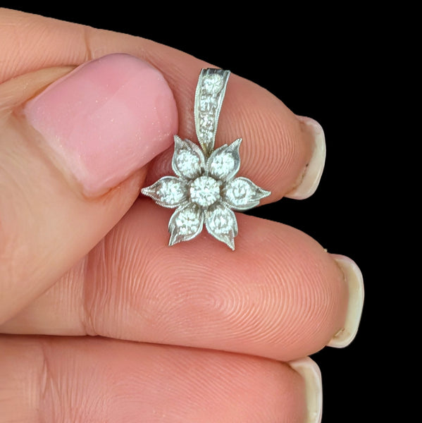 Silver floral pendant held between fingers against a black background