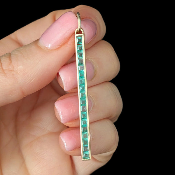 Gold earring with green gemstones held between fingers against a black background